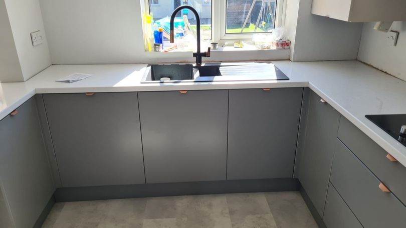Grey matte cupboard with wooden handles, shiny ceramic kitchen and black matte sink